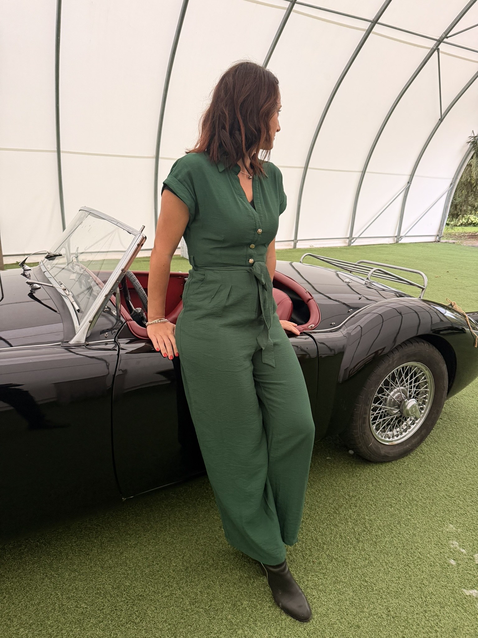 Lena in grünem Overall lehnt an einem schwarzen Oldtimer-Cabriolet mit roten Ledersitzen