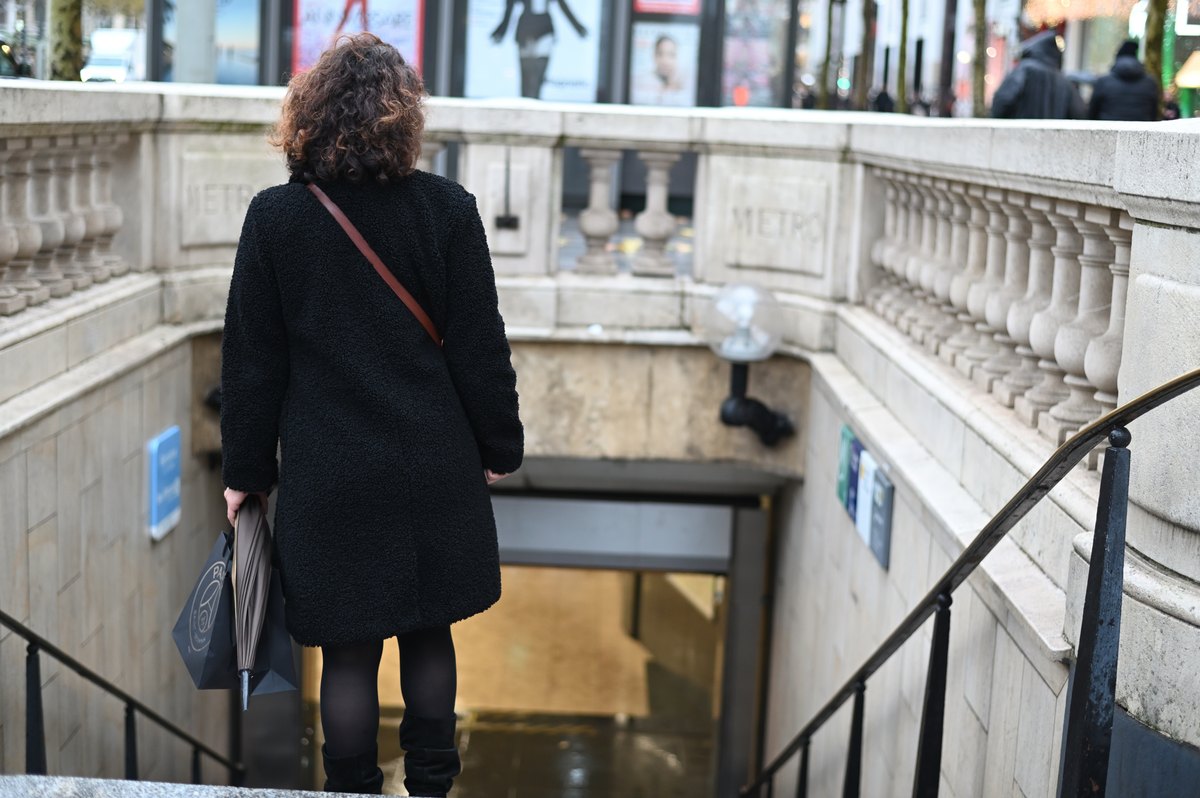 Lena von hinten im schwarzen Mantel, sie geht eine Treppe hinunter